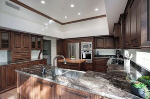 A modern kitchen with dark wood cabinets, granite countertops, stainless steel appliances, and a central island. - Princess Views-Pool & Spa-Walk to TPC Scottsdale (Scottsdale)