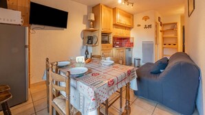A compact kitchen with wooden cabinets, a dining table set for two, and a blue sofa. - Cham Sud Iris361 Near Aiguille du Midi | Balcony Views, Chamonix, France (Chamonix)