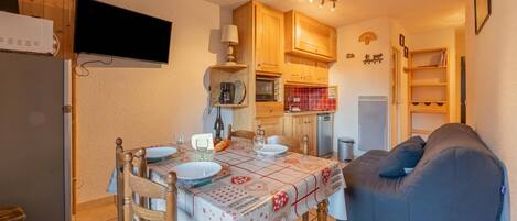 A compact kitchen with wooden cabinets, a dining table set for two, and a blue sofa.