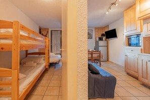 Ein Zimmer mit Etagenbetten, einer Schlafcouch, einem Esstisch und einer Küchenzeile inklusive Schränken und einem Fernseher.