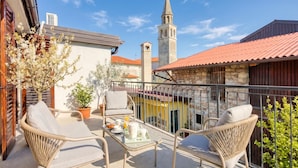 A balcony with wicker furniture, a table with breakfast items, and a view of a church tower. - Vila Leonarda with Terrace and Garden, Miren, Slovenia (Miren)