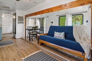 A cozy RV interior with a blue sofa, wooden accents, a dining area, and a view through the windows.