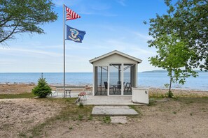A beachside gazebo with a clear view of the ocean, a flagpole with an American flag, and a small tree.