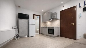 Eine moderne Küche mit Einbauofen, Kühlschrank und Mikrowelle. Eine Holztür und ein kleines Fenster sind ebenfalls vorhanden.