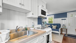 Una cocina moderna con armarios blancos, un lavamanos de acero inoxidable y una estufa. En la zona de estar contigua hay un sofá azul.