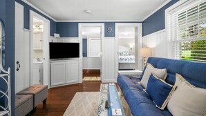 Una sala de estar con un sofá azul, un televisor de pantalla plana y un comedor con armarios blancos y una encimera de cocina.