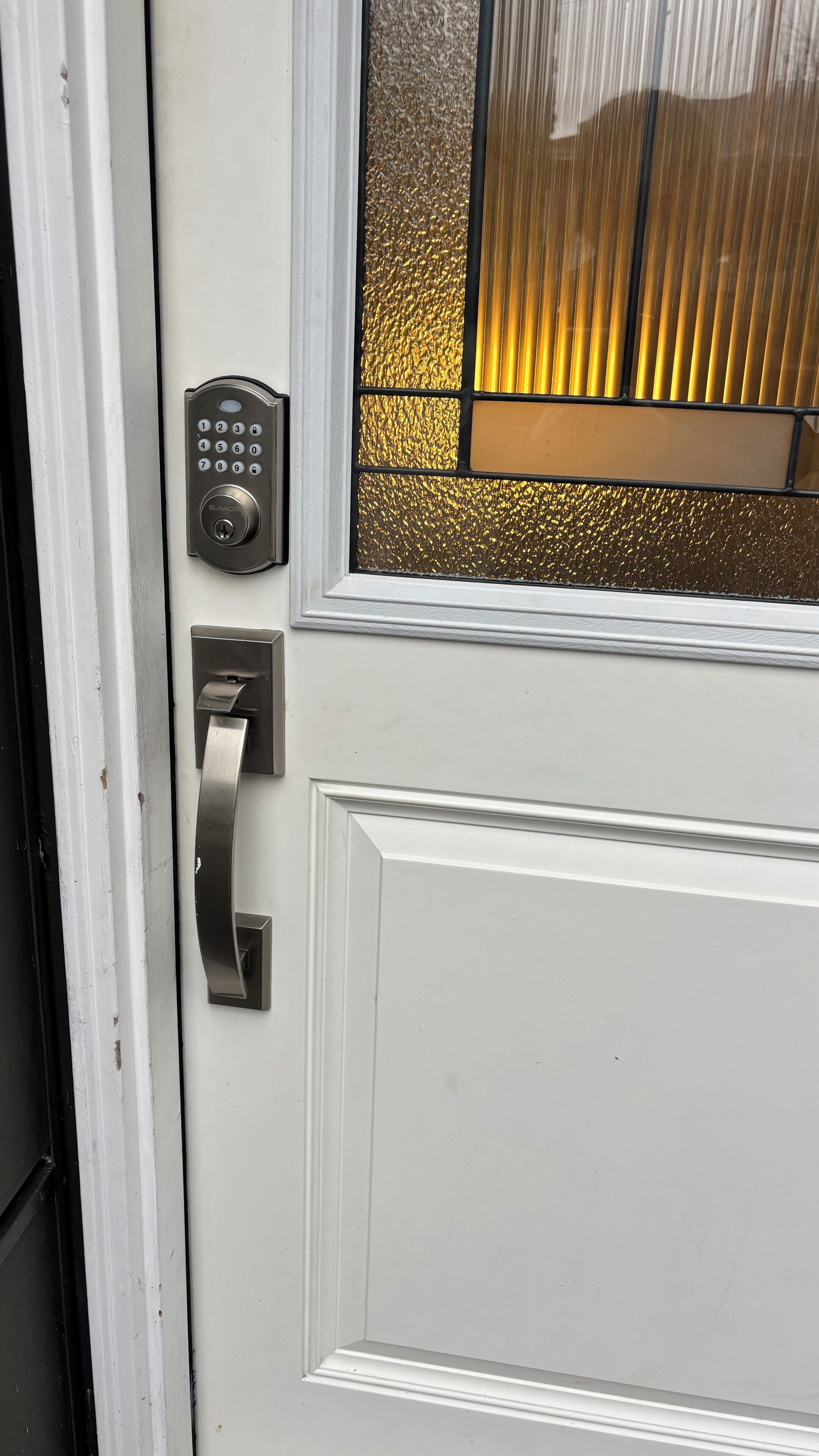 A white door with a keypad lock, a doorbell, and a frosted glass window.