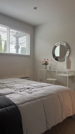 A bedroom with a bed, a white dresser, a round mirror, and a window with blinds.