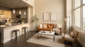A modern kitchen with a central island, bar stools, a sofa, and a coffee table. There is a window providing natural light and a view of the outdoors. - Boulevard Stays Midtown 30ft Ceilings 1BR 01 (Nashville)