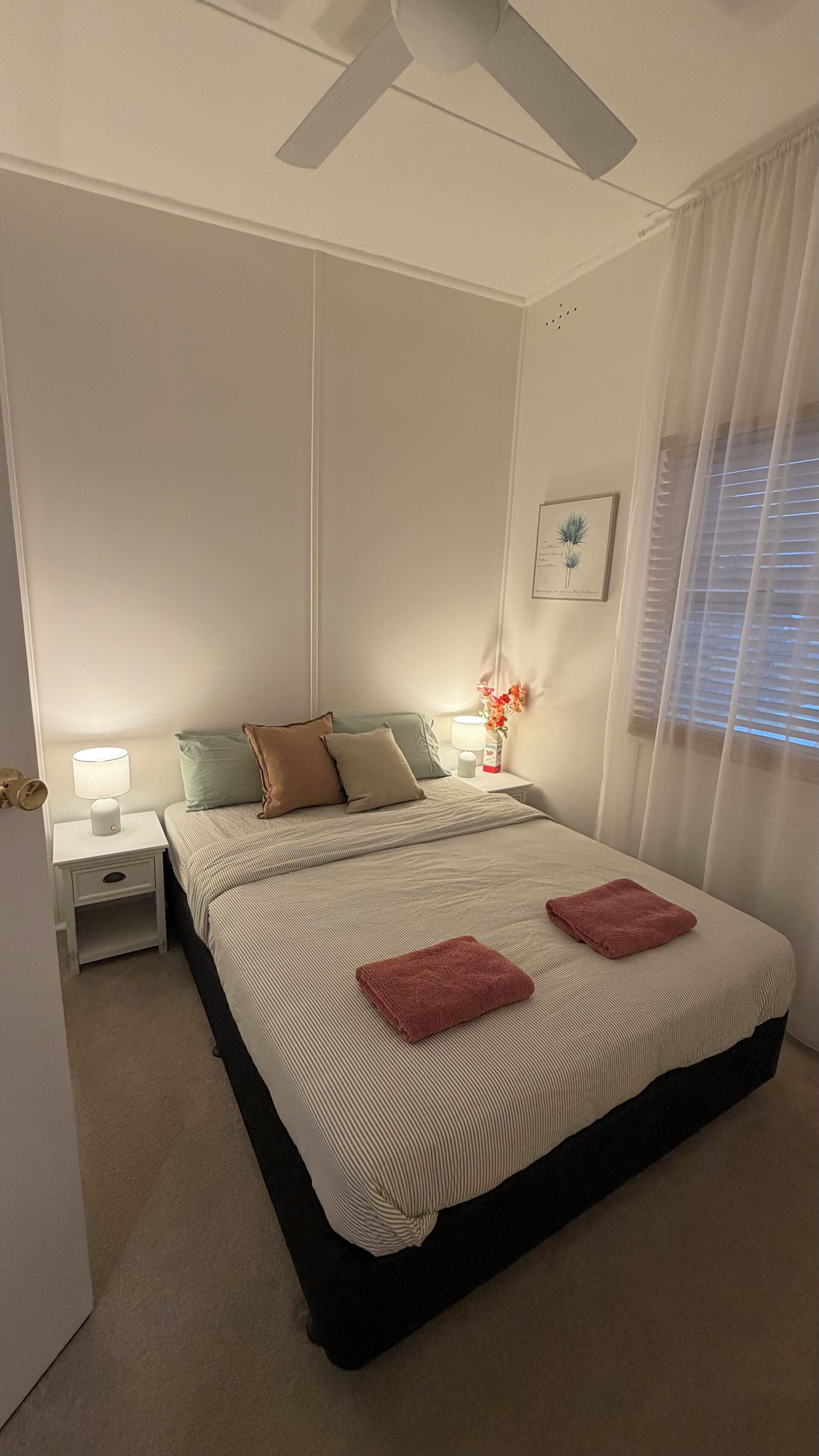 Ein Schlafzimmer mit einem Bett, Nachttischen, einem Deckenventilator und einem Fenster mit Vorhängen.