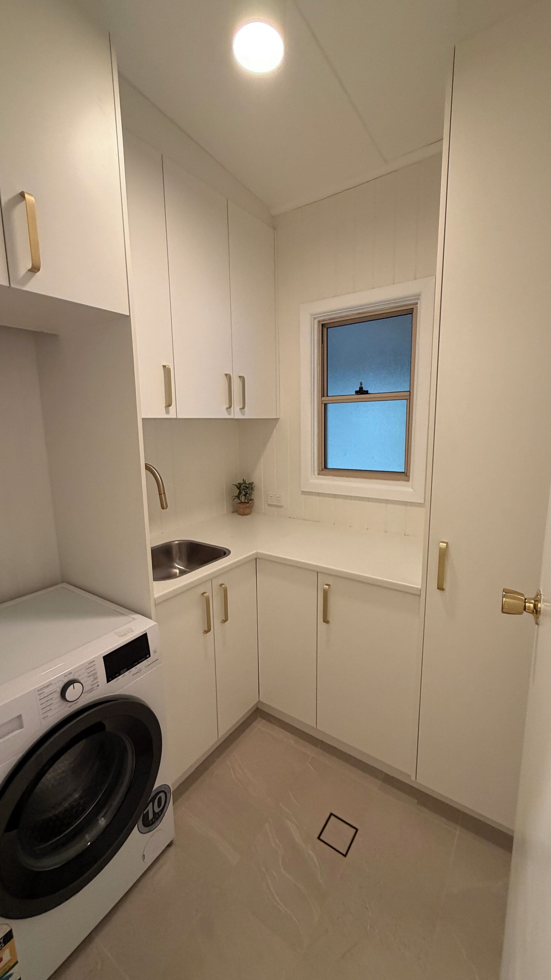 Ein kleiner Hauswirtschaftsraum mit Waschmaschine, Spüle und einem Fenster mit Blick.