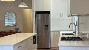Una cocina moderna con armarios blancos, un refrigerador de acero inoxidable, una estufa a gas y piso de madera.