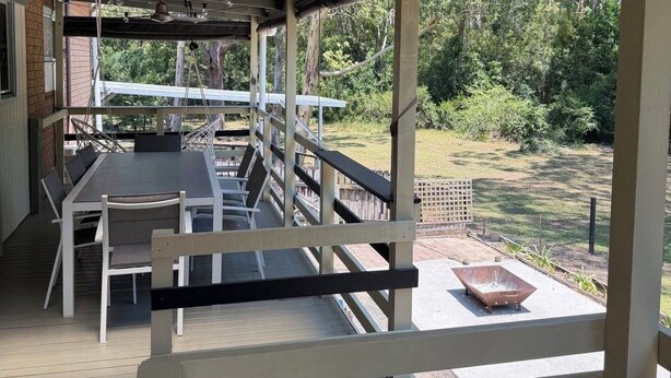Eine Terrasse im Freien mit Tisch und Stühlen, einem Metallzaun und Blick auf einen bewaldeten Bereich.