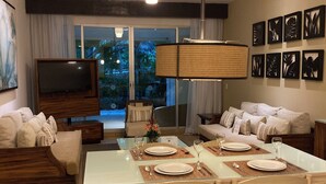 Un salon moderne comprenant un coin repas, un téléviseur et un balcon offrant une vue sur l’extérieur.