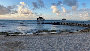 Une plage avec deux constructions à toits de chaume qui s’avancent dans la mer.