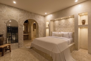 A bedroom with a stone wall, a bed, a bench, and a shelf with a vase. - Bohemian 2BR Private Suites By Orivista (Kerobokan)