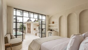 A spacious bedroom with a large bed, a seating area, and a view of a pool and outdoor area. - Bohemian 2BR Private Suites By Orivista (Kerobokan)