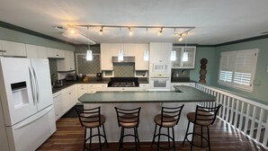 Een moderne keuken met witte kasten, een centraal eiland met barkrukken, een magnetron en een fornuis.