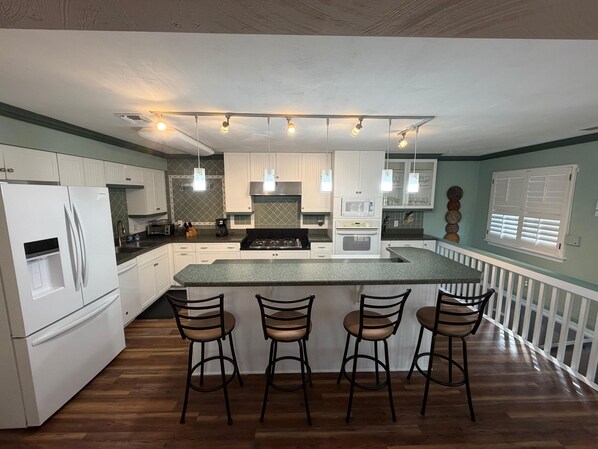 Een moderne keuken met witte kasten, een centraal eiland met barkrukken, een magnetron en een fornuis.