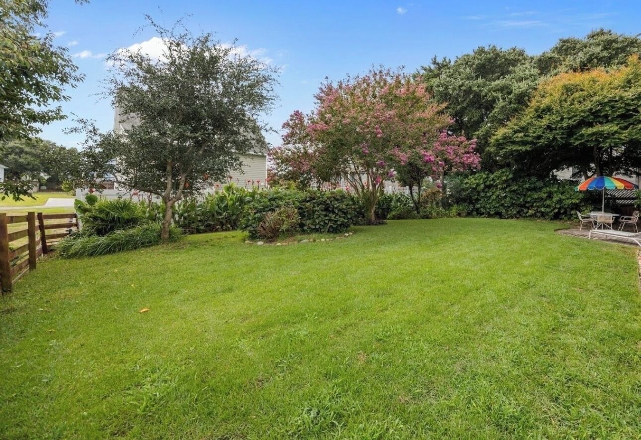 A well-maintained grassy yard with a wooden fence, various shrubs, and trees.