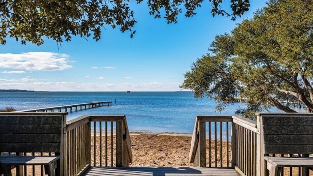Een houten terras dat uitkomt op een strand, met een helder uitzicht over de oceaan en een boot in de verte.