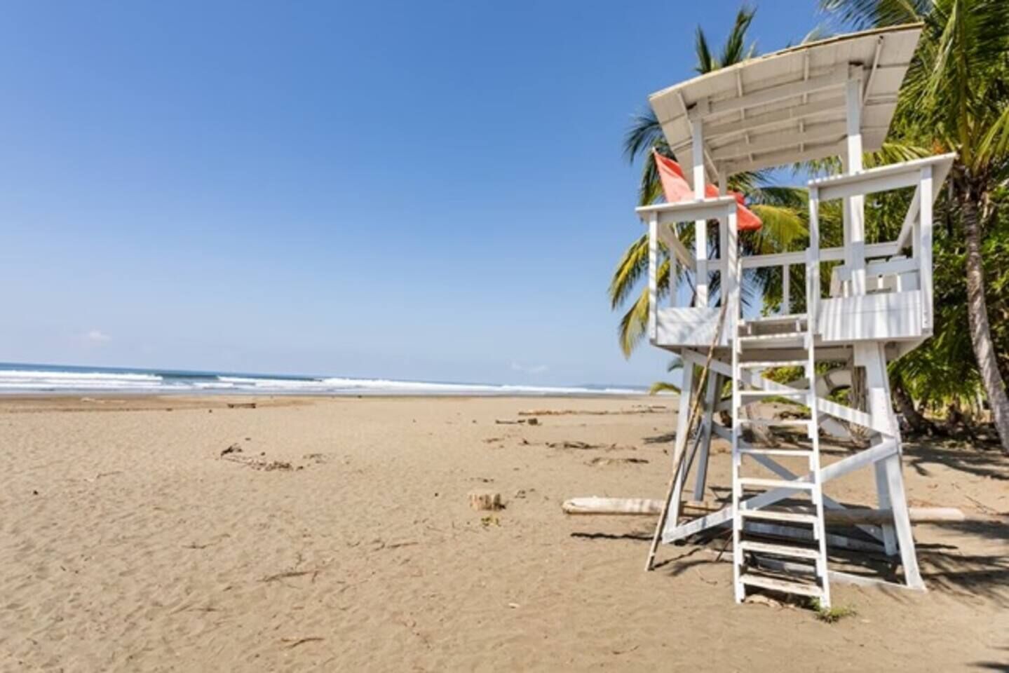 A beach with a lifeguard tower and palm trees.