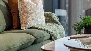 Una sala de estar moderna con un sofá verde, una mesa redonda y un ventanal con vistas a edificios.