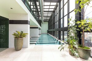 Un ambiente interno moderno con una scala in vetro, piante in vaso e vista sulla città.