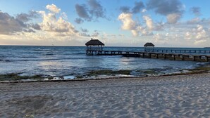 En strand med två byggnader som har tak av halmtak och som sträcker sig ut i havet.