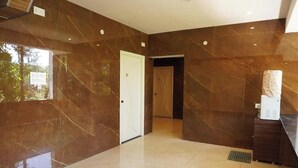 A hallway with marble walls and a tiled floor, leading to a door and a reception area. - Shree Mantra Residency  (Yercaud)