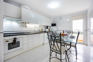 Una cocina moderna con armarios blancos, horno integrado y comedor con mesa y sillas de vidrio.
