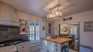 Una cocina moderna con armarios blancos, una isla central y un comedor con sillas de mimbre.