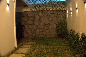 A stone wall with a metal fence, a concrete pathway, and a small bush.