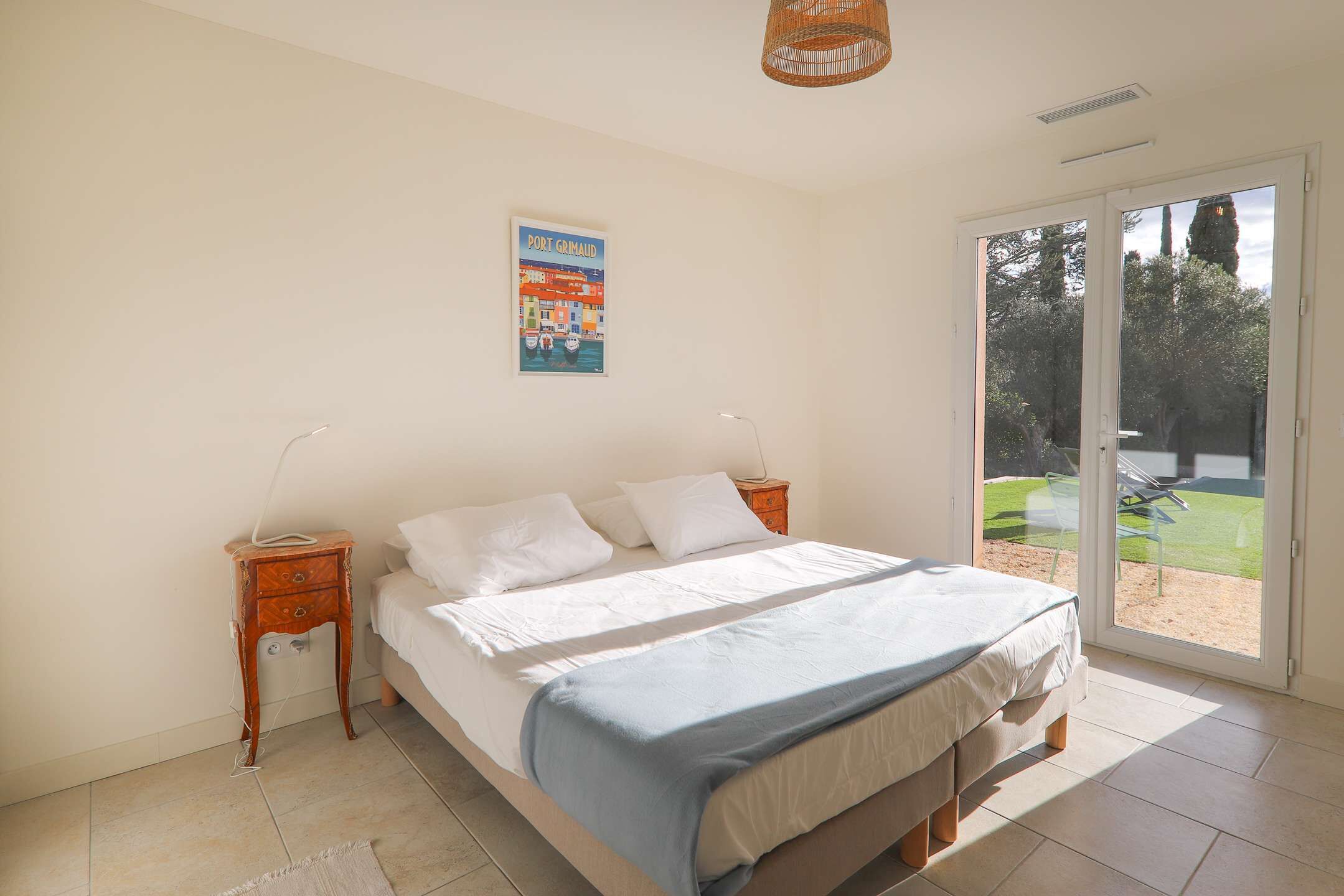 Un dormitorio con cama, mesita de noche, un cartel en la pared y puerta corrediza de vidrio que da a un espacio exterior.
