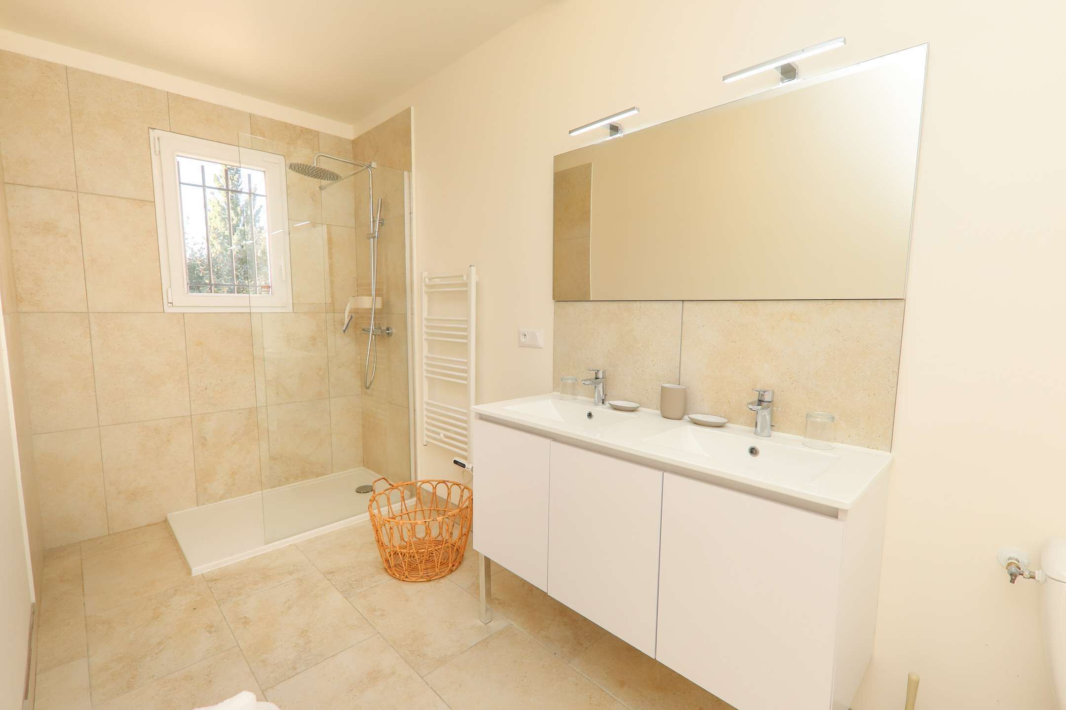 Un baño moderno con cabina de ducha, un espejo grande y un tocador blanco con dos lavamanos.