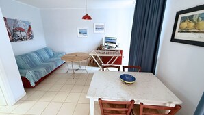 Un espacio habitable compacto con una mesa de comedor, sillas, un sofá, un televisor pequeño y una computadora.