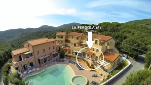 Un complejo turístico con piscina, varias edificaciones y montañas al fondo.