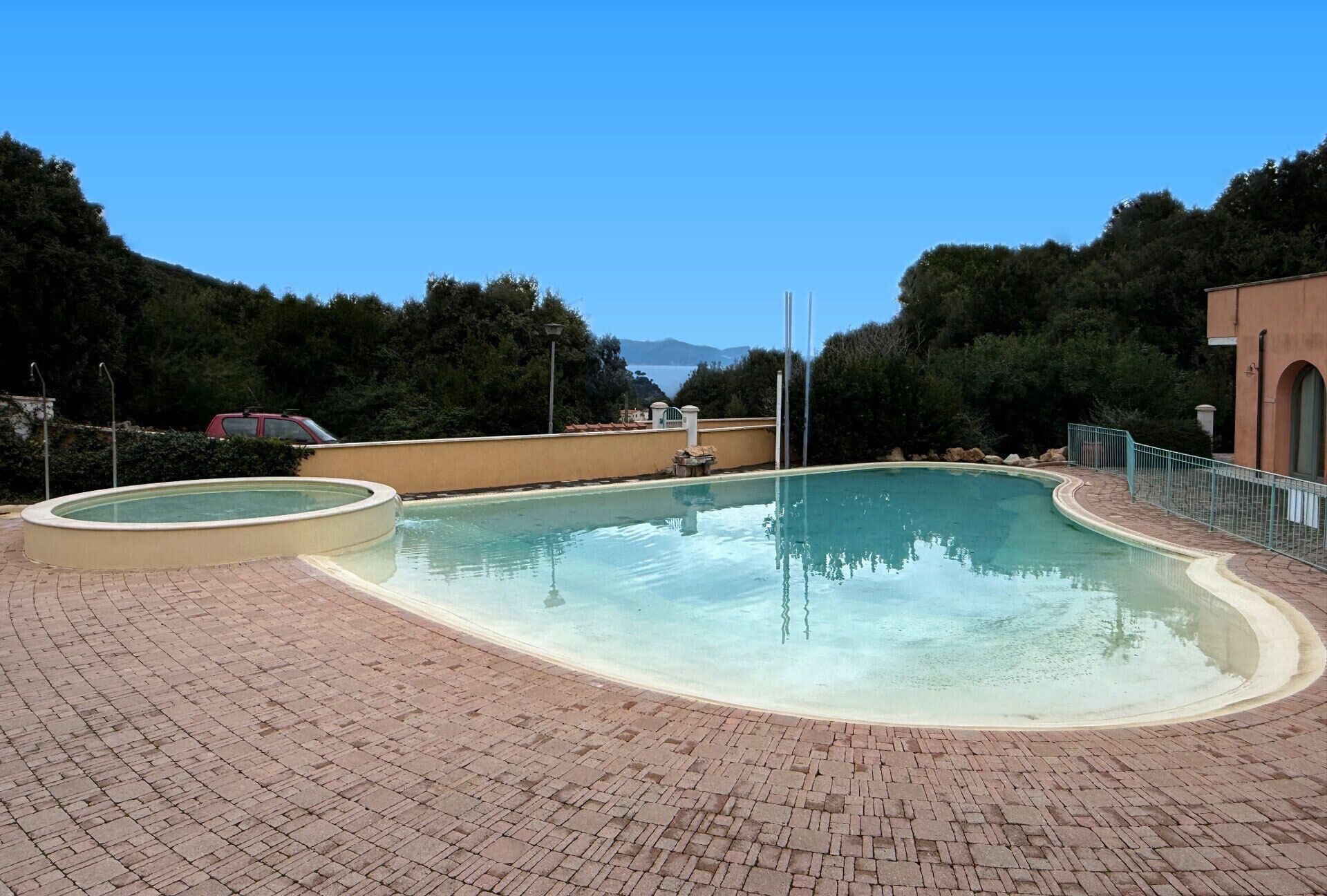 A swimming pool with a curved edge, surrounded by a brick patio.