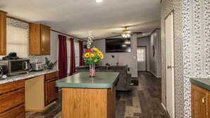 Una cocina con armarios de madera, un microondas y un lavamanos. Hay un comedor con una mesa y sillas.