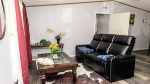 Una sala de estar con un sofá de cuero, una mesa de centro de vidrio y una planta pequeña en una mesita auxiliar.