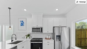 A modern kitchen with white cabinets, stainless steel appliances, a dishwasher, and a large window offering a view of the outdoors. - Spacious Modern Home w/ Smart Entry (Houston)