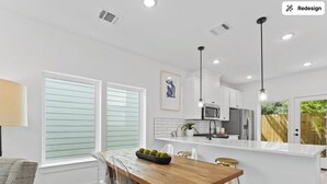 A modern kitchen with white cabinetry, a wooden dining table, and a bar area. - Spacious Modern Home w/ Smart Entry (Houston)