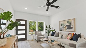 A spacious living room with a sofa, coffee table, and chairs. There is a large window with a view of greenery outside. - Spacious Modern Home w/ Smart Entry (Houston)