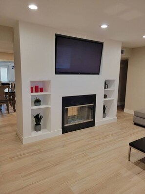 A modern living room with a flat-screen TV mounted above a fireplace, surrounded by white shelving units. - Four Bedroom Home with Swimming Pool and Game Room (Lake Havasu City)