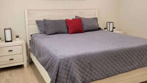 A bedroom with a bed, a nightstand, a bedside table, and a wall-mounted picture. - Four Bedroom Home with Swimming Pool and Game Room (Lake Havasu City)