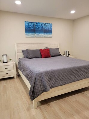 A bedroom with a bed, a nightstand, a bedside table, and a wall-mounted picture. - Four Bedroom Home with Swimming Pool and Game Room (Lake Havasu City)