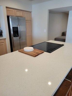 A kitchen with a stainless steel refrigerator, a wooden cabinet, a countertop, and a black induction cooktop. - Four Bedroom Home with Swimming Pool and Game Room (Lake Havasu City)