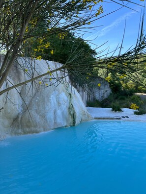 Piscina com águas azuis cristalinas, rodeada por formações rochosas brancas e vegetação.