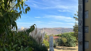 Un patio con mesa y sillas, rodeado de vegetación y vistas a colinas distantes.