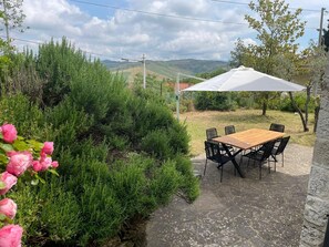 Um pátio com mesa e cadeiras, cercado por vegetação e vista para colinas.